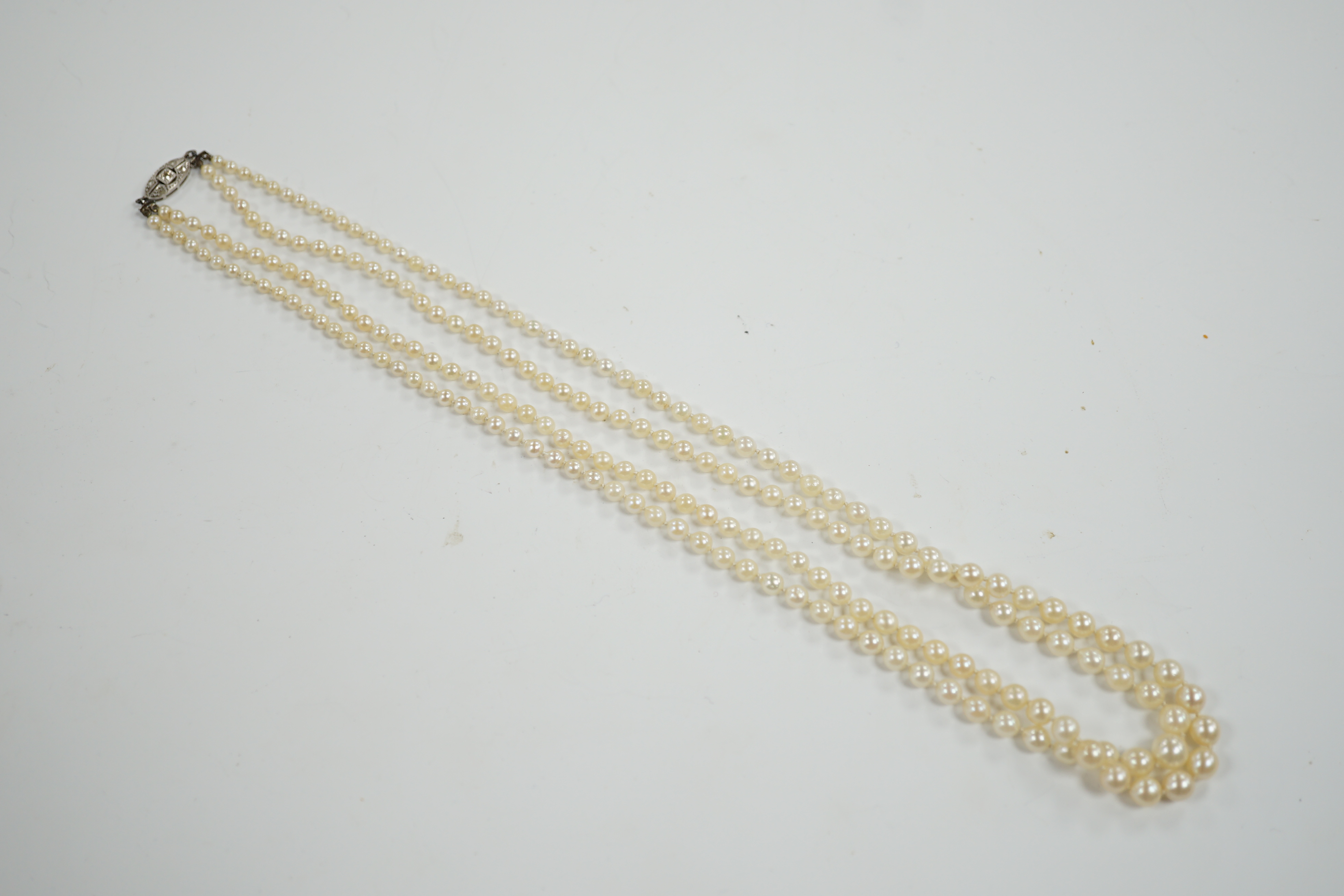 A 1930's twin strand graduated cultured pearl necklace, with 14ct, plat and diamond chip set clasp, 50cm.